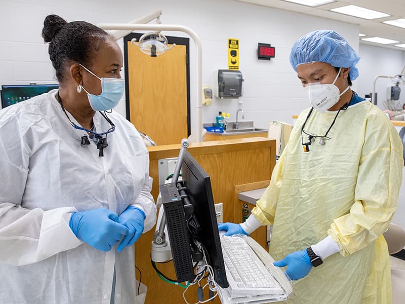 Dr. Joann Travis, left, a faculty member who practices at the G.V. “Sonny” Montgomery Veterans Affairs Medical Center, reviews the record of a patient in the Restorative Clinic with fourth-year student Stan Tristeza before hebegins treatment.